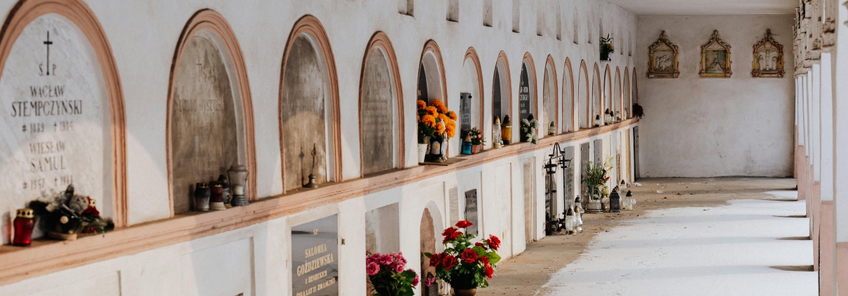 Quiet corridor in a cemetery with rows of tombs decorated with flowers and candles.