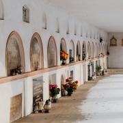 Quiet corridor in a cemetery with rows of tombs decorated with flowers and candles.