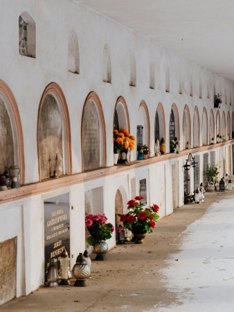 Quiet corridor in a cemetery with rows of tombs decorated with flowers and candles.