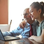Elderly man and young woman bonding while using a laptop indoors.