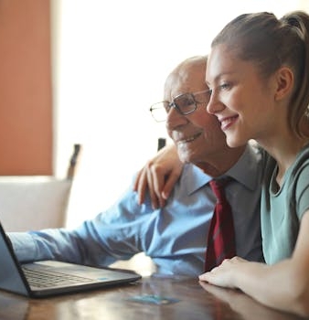 Elderly man and young woman bonding while using a laptop indoors.