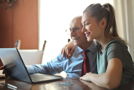 Elderly man and young woman bonding while using a laptop indoors.